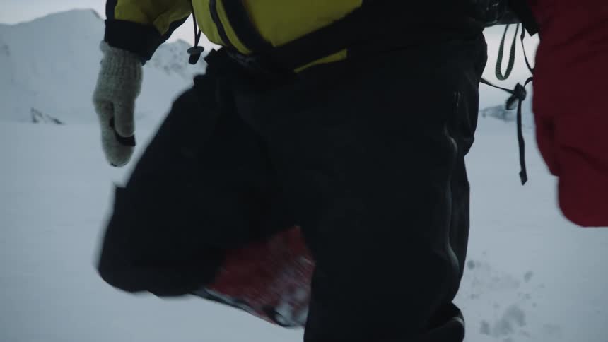 Man with yellow coat red gloves and black pants hikes through snow on the mountain