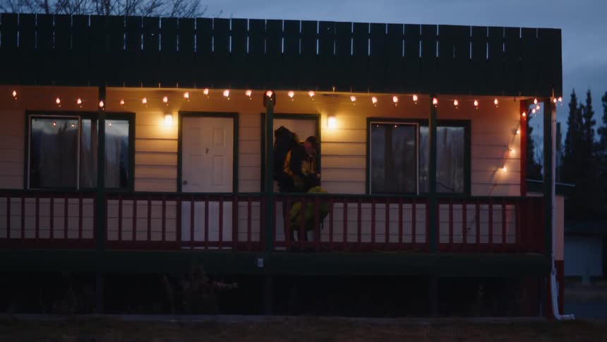 Man carrying large backpacks exits a motel room at morning