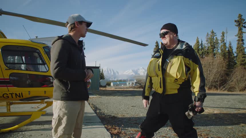 Two men talking to each other outside next to a helicopter on pavement