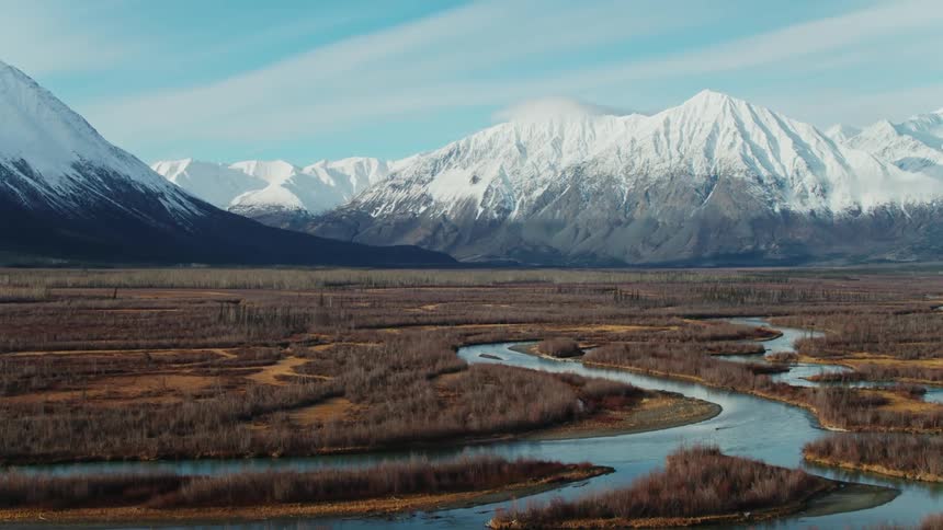 An aerial view of a winding river valley with a mountain range in the background