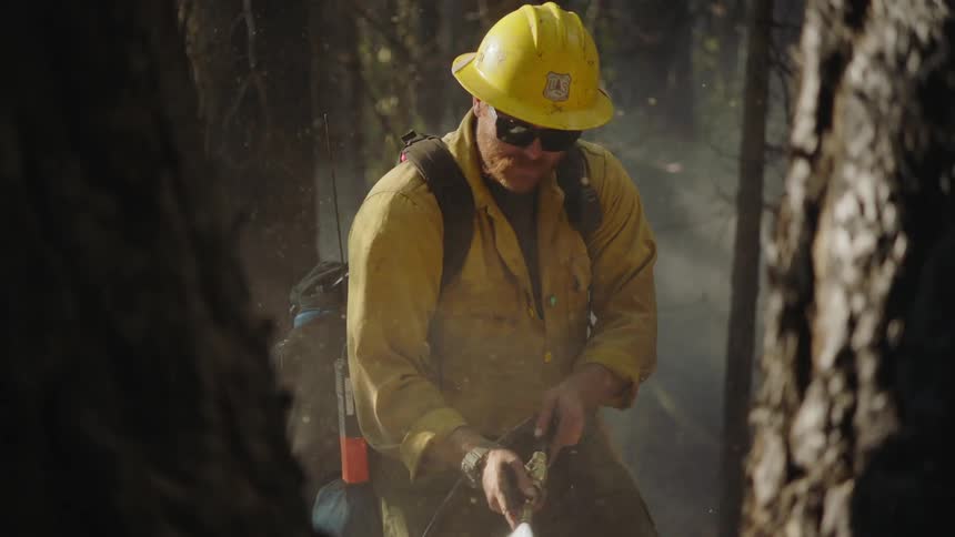 Firefighter wearing yellow protective gear hoses the ground on the forest