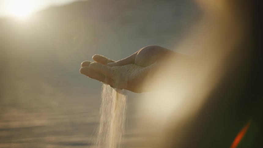 A man on the the desert letting a handful of sand fall through his fingers at sunset