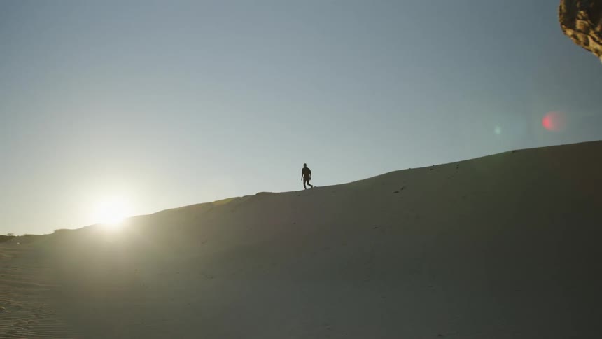 Silhouette of a man walking over the ridge of a dune at sunset