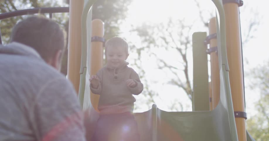 A little boy slides down a slide and into his father's arms