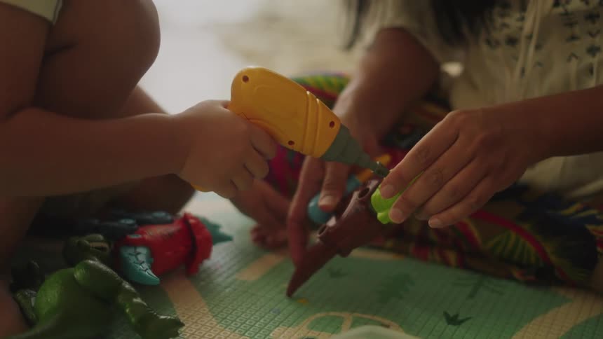 A close up of a mother and song playing with toys on the floor as the child reaches for another