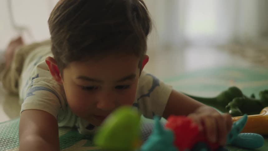 A young boy laying on the floor playing with dinosaur toys