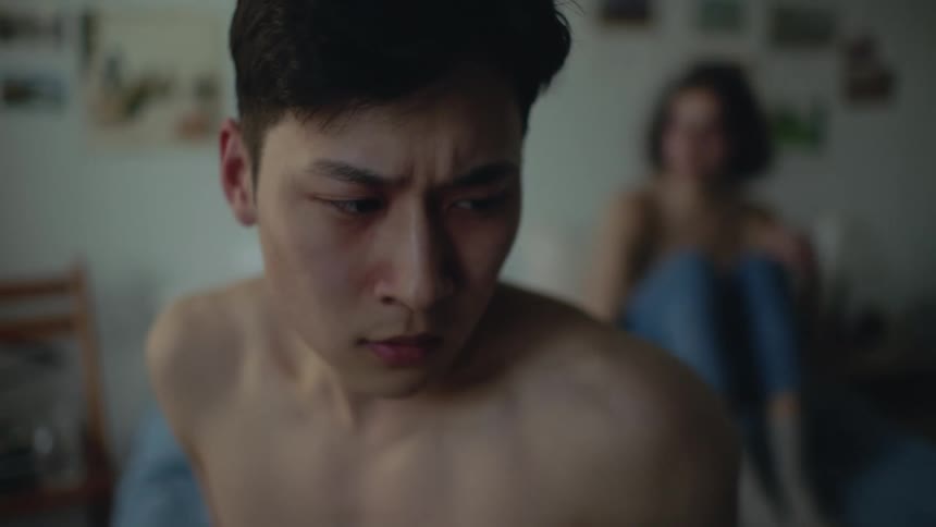 A man looks perturbed after jumping off the bed where a woman sits