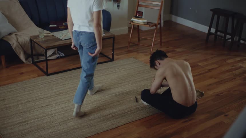 Young woman sits on the floor of the living room to console a young sad shirtless man