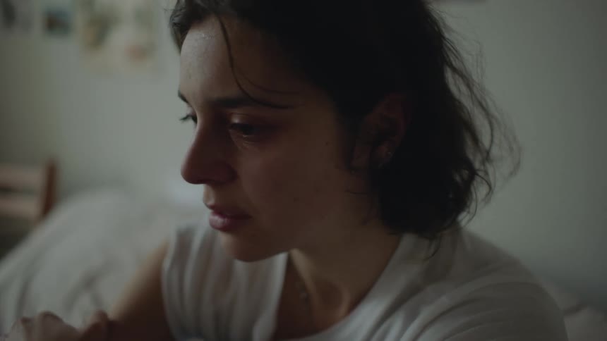 A female is crying and sitting in her bedroom