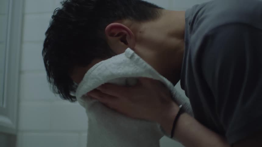 A man washing his hands in the sink grabbing a towel wiping his face with it and looking down