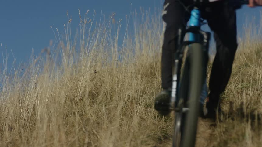 Cyclist rides down grassy slope under a clear blue sky