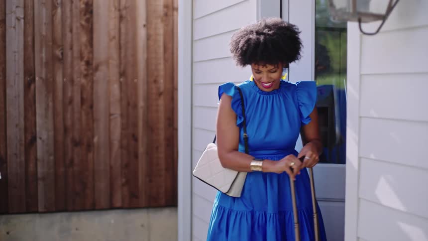 A woman is leaving her house with a suitcase