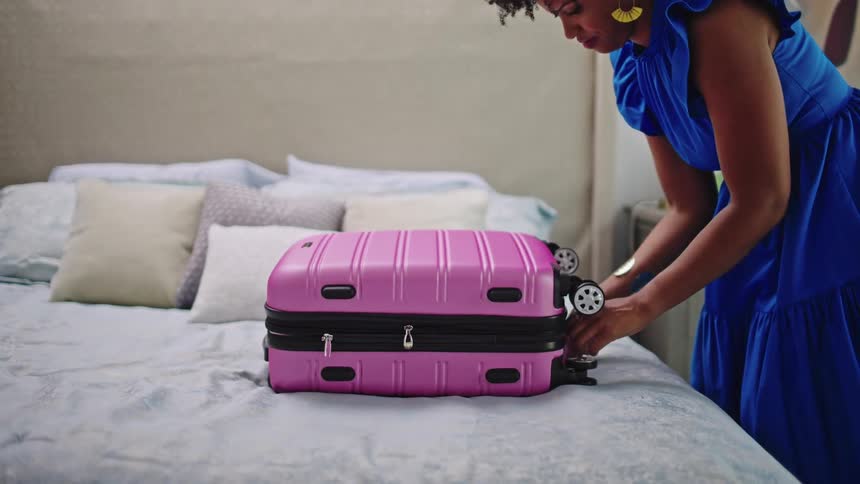 A woman packing a pink suitcase in front of her on the bed and then zipping it up and walking away