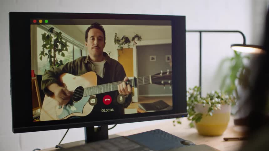 Woman plays musical keyboard while guitarist plays on monitor during video meeting