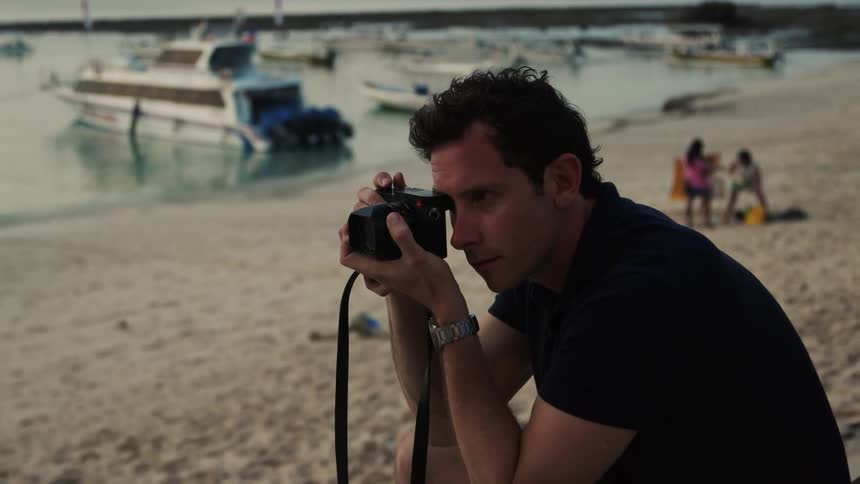 Man with black t shirt and silver wristwatch takes photo with camera on the beach
