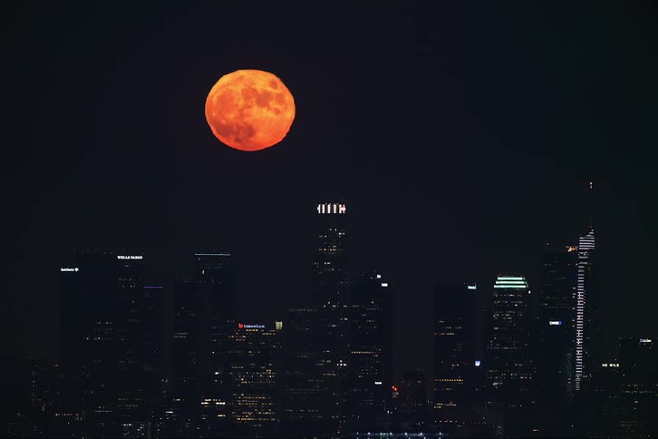 A time lapse of a city lit up at night as a full red moon raises in the sky over the city