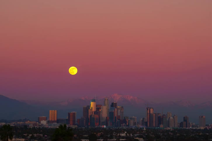 Time lapse of the full moon rising in the sky and city skyline