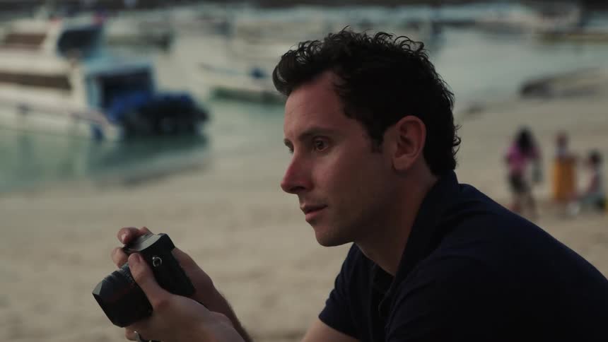 Man in black shirt and wristwatch takes photo with camera on the beach at sunset