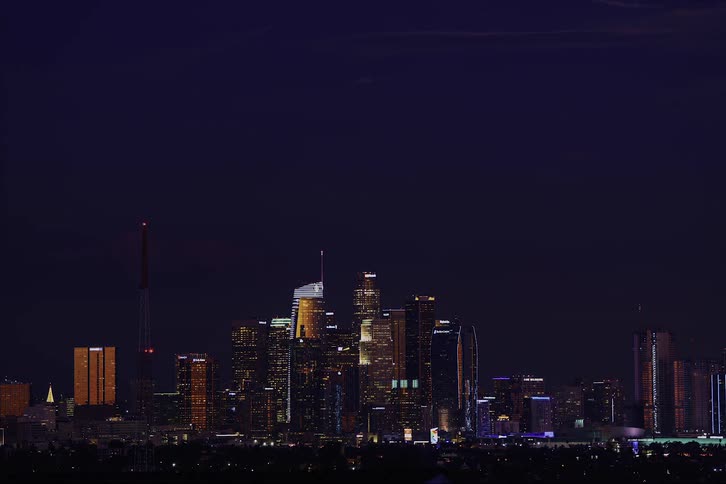 A landscape view of the full moon rising up in the night sky over a busy urban city skyline