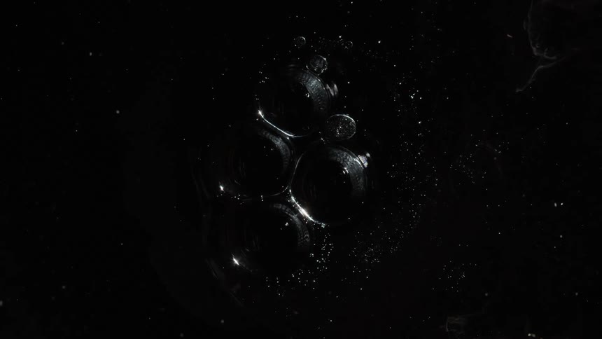 Particles swirl around cluster of large bubbles against a black background