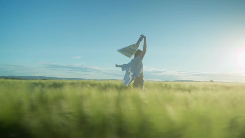 Young woman holding a bag on her hand runs on field of tall green grass at morning