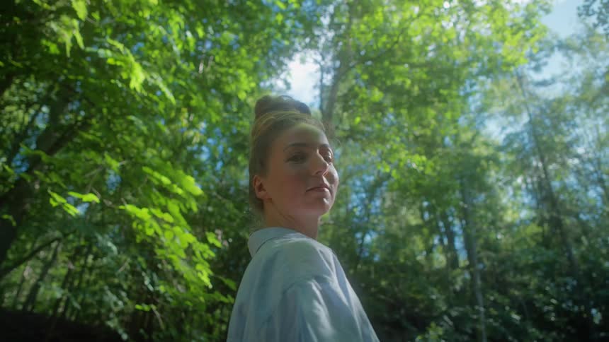 A teenage girl is standing near the woods as she turns her head on a sunny day