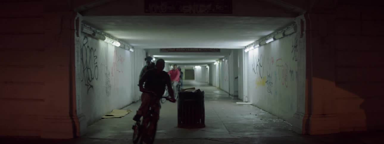 Four young men riding their bicycles through a tunnel with graffiti on the walls