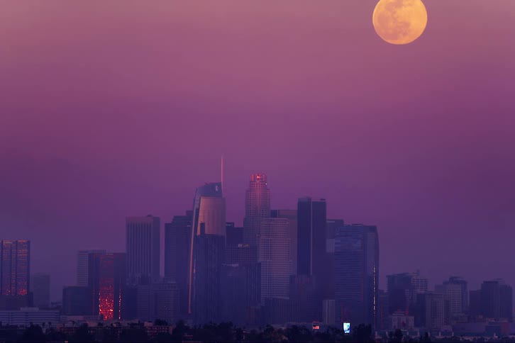 Full moon rises behind city skyline in purple sky
