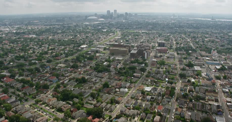4K aerial footage tilts up from suburban neighborhoods to reveal the towering skyscrapers of Downtown New Orleans under partly cloudy skies