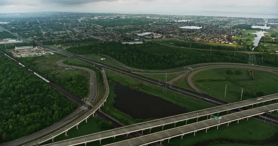 Fly over highway interchange to approach a Louisiana suburb at sunrise capturing the city and residential neighborhoods in a partly cloudy sky