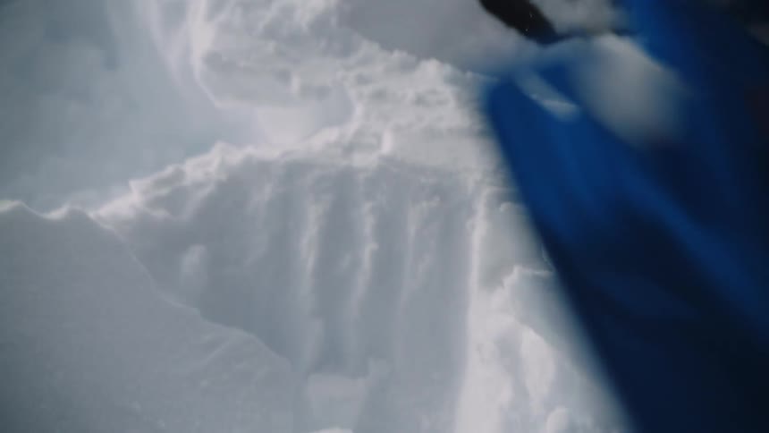 Close up of a person using a small blue shovel to dig in snow