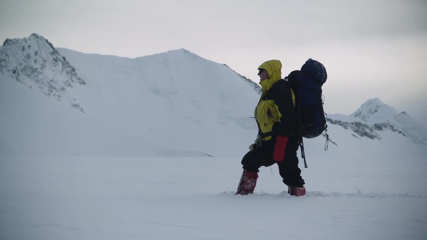 A person wearing winter gear treks through white snow in the mountains