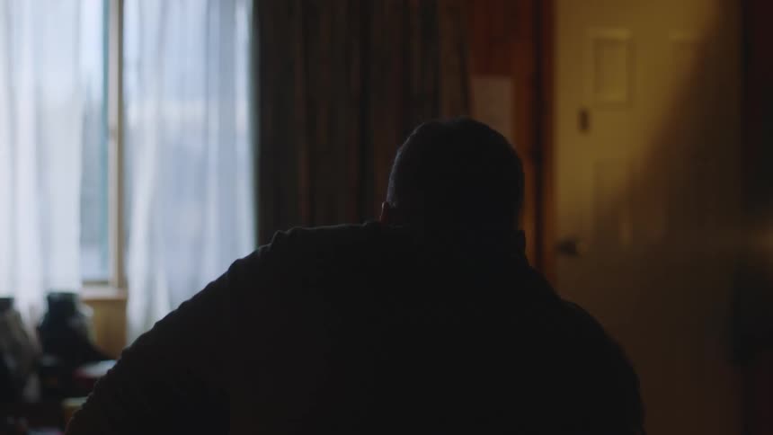 Man sitting on bed is silhouetted against the windows in bedroom