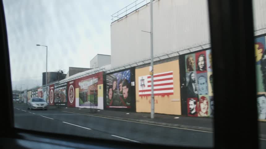 Many murals on a wall next to a busy city street