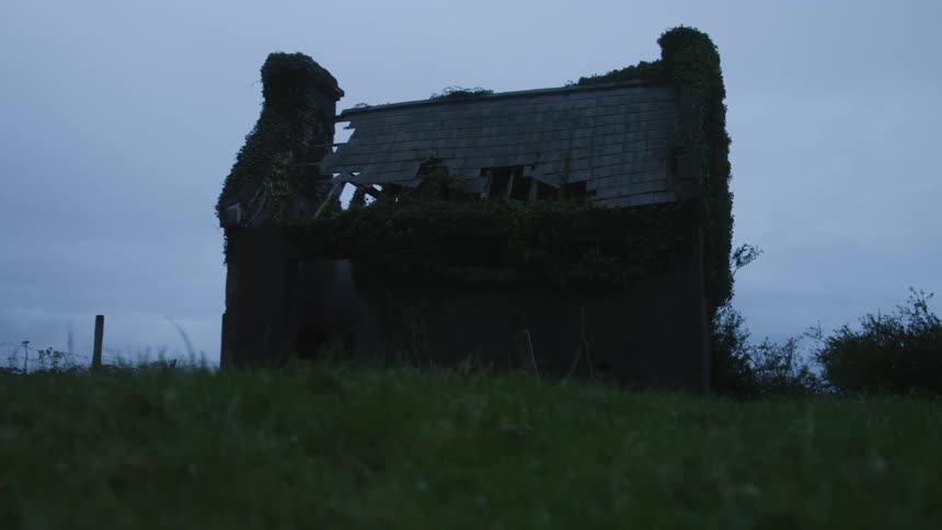 A twostory abandoned house with a chimney and a collapsed roof appears under a cloudy sky