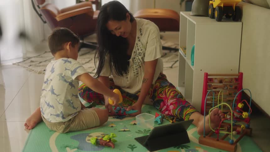 Mother and son sitting on floor play with toys together in the living room