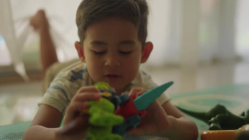 Boy lying on the floor plays with toys in the living room at home
