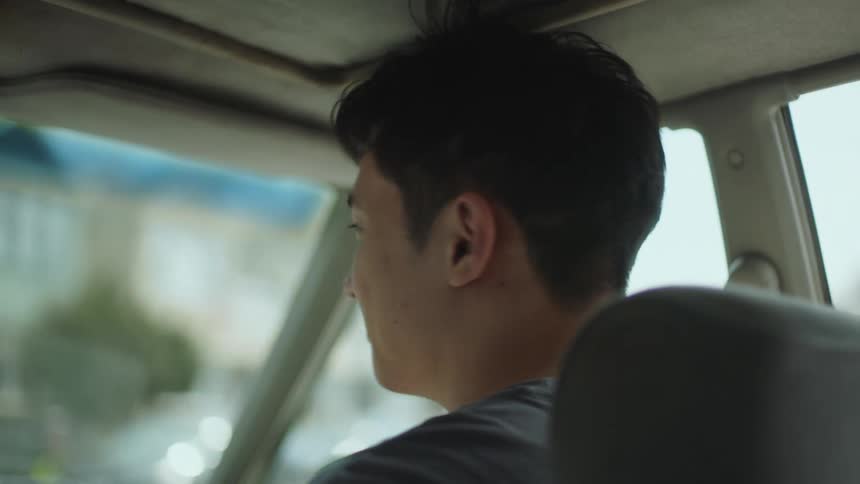 A close up of a mans face smirking as he rides in the passenger seat of a car