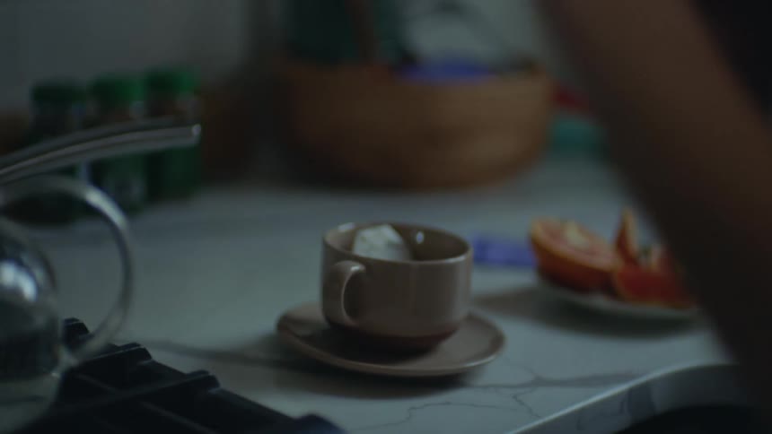 A young woman in the kitchen boils water on the stove opens a tea packet and adds honey to a cup