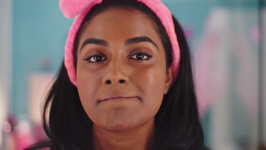 A close up of a woman wearing a pink head band applying pink lipstick to her lips