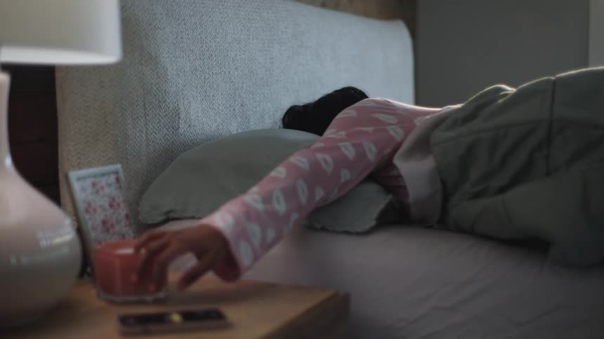 Woman sleeping with her back to the camera grabs a ringing phone from the night stand
