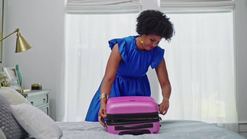 Woman packing blue blazer into a bright pink rolling suitcase