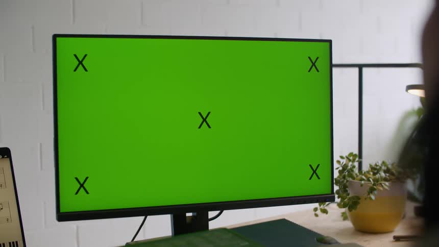 Someone sitting at a desk is looking at a computer monitor that has a green background and a pattern of black xs
