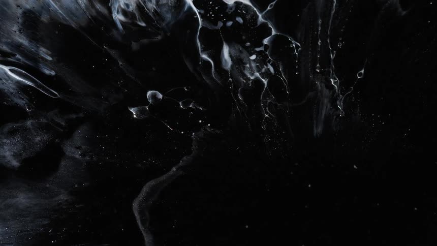 Close up of strands of white liquid ink floating on a dark background