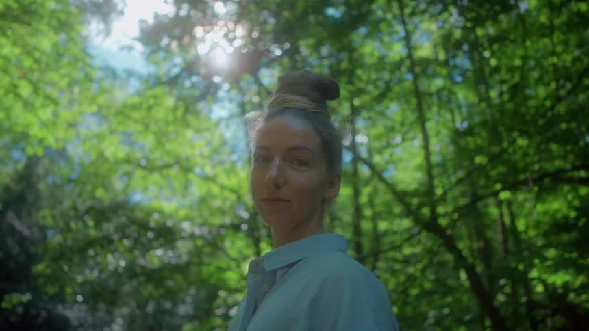 Portrait of a woman standing in the woods under tall green trees