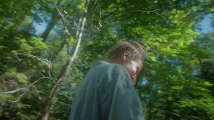 Blonde woman with light blue shirt and shorts happily runs in the green forest