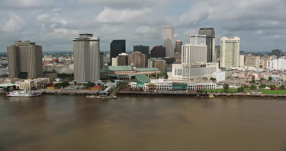 Aerial footage of Downtown New Orleans reveals the riverfront skyscrapers and a cruise ship on a partly cloudy day