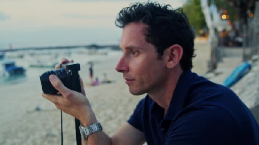 A man is sitting on the beach and taking pictures