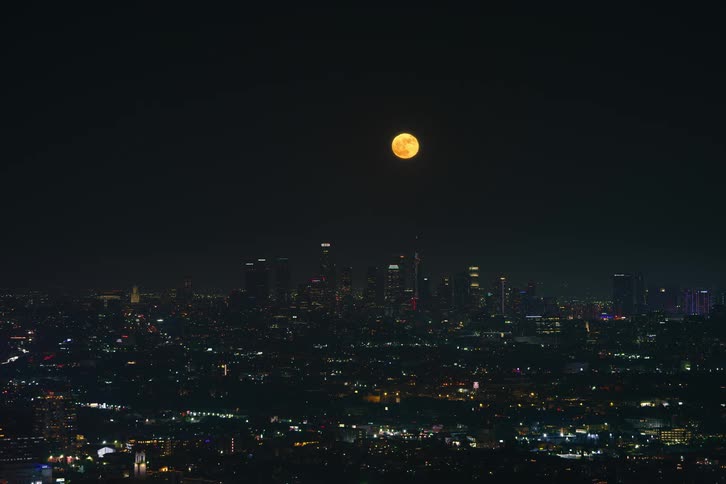 An aerial view of the night sky and a full moon rising over a lit up city skyline