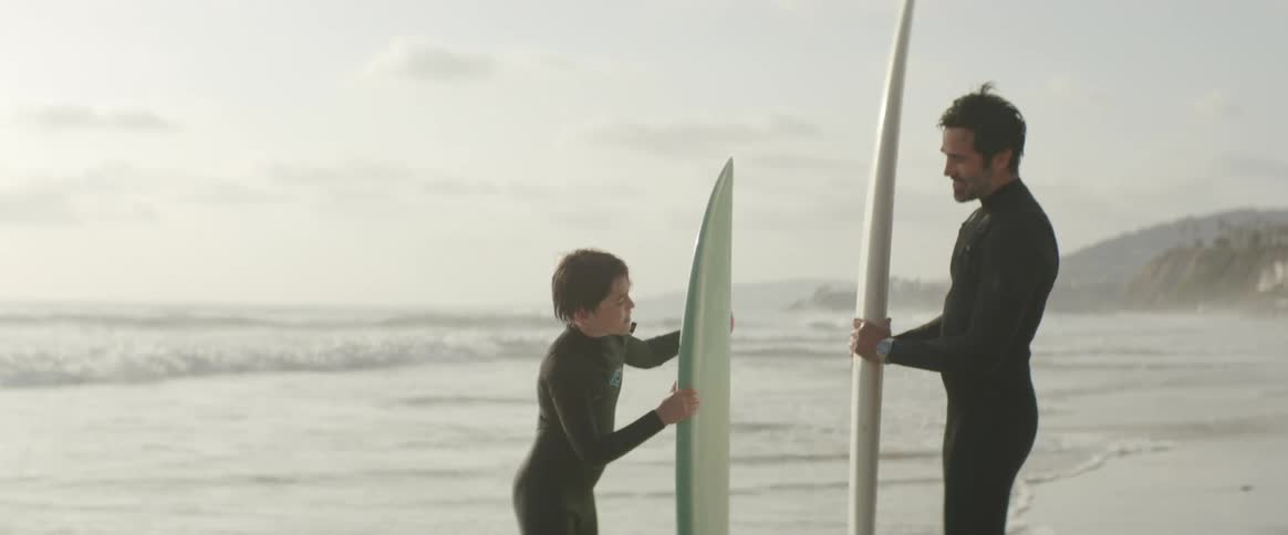 Father and son holding surfboard at shoreline on a hazy day at the beach